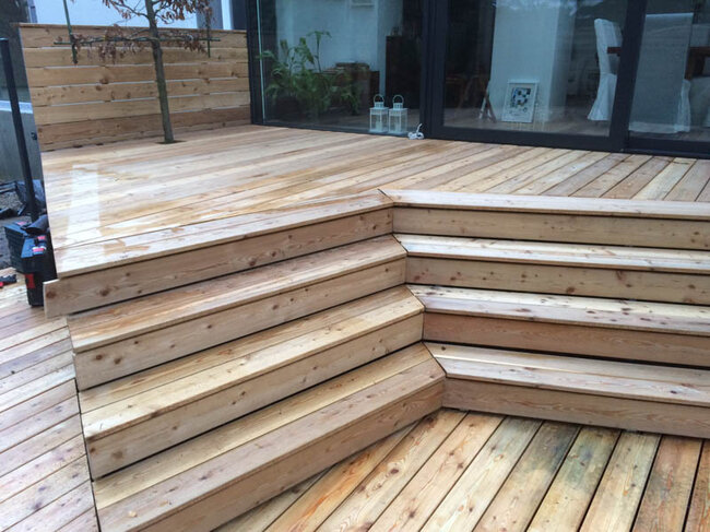 Moderne Holzterrasse mit Ecktreppe und Glasschiebetüren