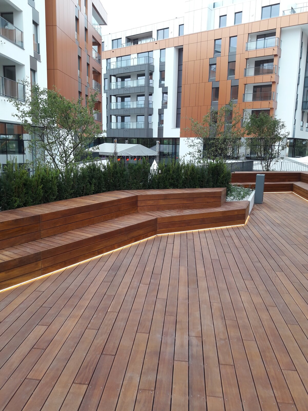 Moderne Terrasse mit Holzbänken und LED-Beleuchtung vor dem Hintergrund von Apartmenthäusern