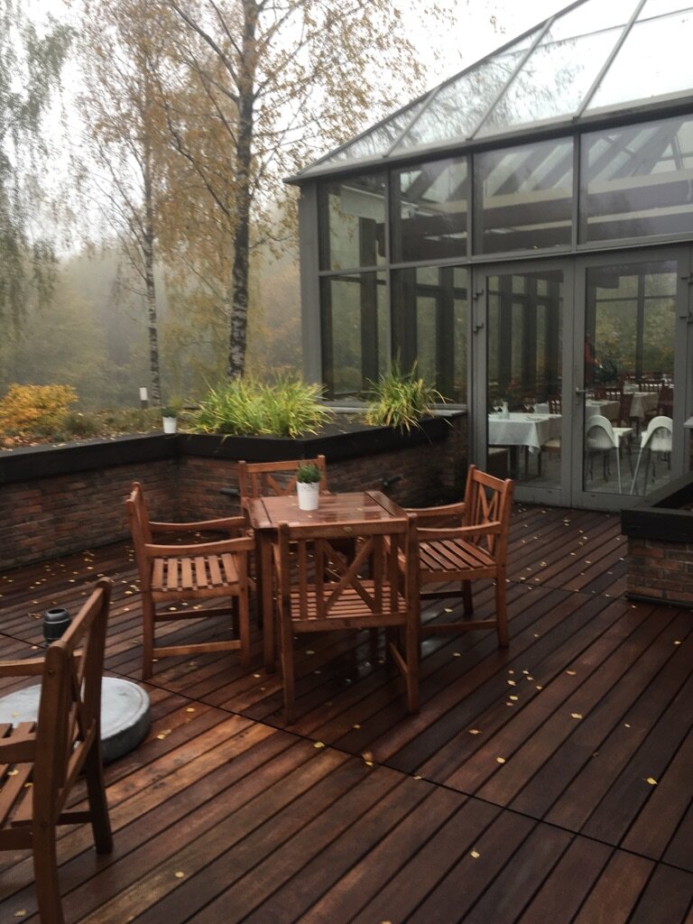 Holzterrasse im Garten mit Möbeln und Wintergarten im Hintergrund