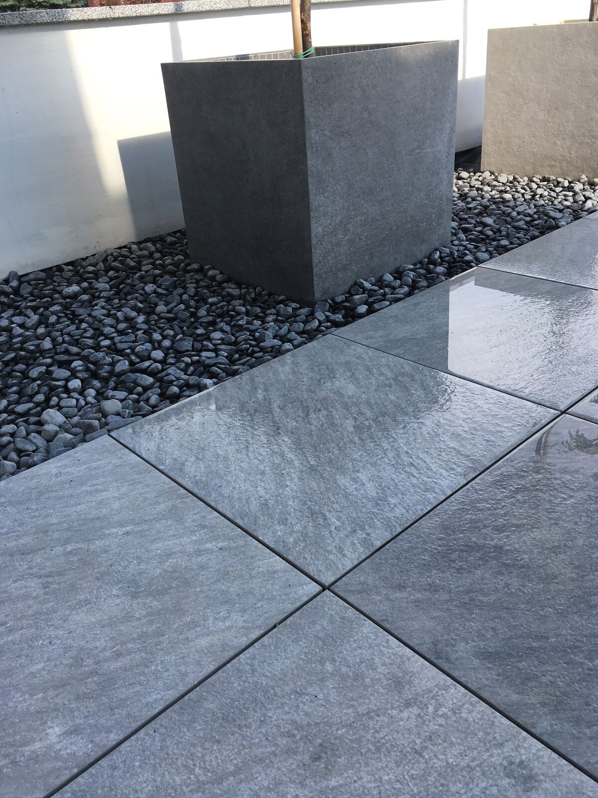 Graue Platten auf der Terrasse mit Steinumrandung und Pflanzgefäß