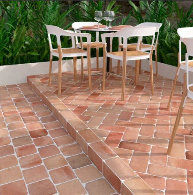 Taras z terrakoty z meblami ogrodowymi i zielenią w tle