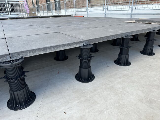 Foto einer Stelzlager Terrasse während der Montage mit höhenverstellbaren Stelzlagern und Balken sowie WPC-Dielen.