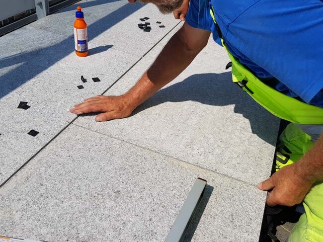 Ein Mann verlegt Terrassenplatten auf höhenverstellbaren Stelzlagern auf einer Terrasse.