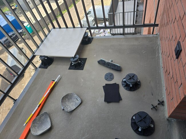 Die erste verlegte Platte auf dem Balkon nach dem Ausrichten auf einem höhenverstellbaren Stelzlager Standard