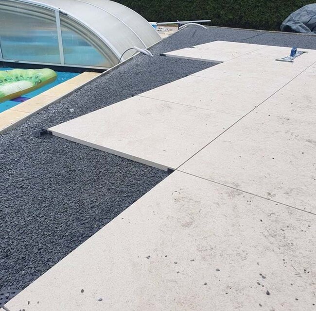 Laying light terrace pavers on supports on a gravel base by the pool.