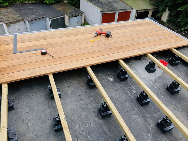 Verlegung einer Holzterrasse auf Balken und verstellbaren Stelzlagern.