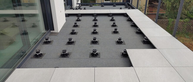 Montage einer Stelzlager Terrasse aus hellgrauen Feinsteinzeugplatten auf schwarzen höhenverstellbaren Stelzlagern.