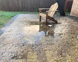 Große Pfütze auf der Terrasse aus Pflastersteinen aufgrund schlechten Wasserabflusses.