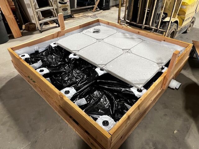 Großer hölzerner Stelzlagerrahmen mit schwarzer Kunststoffauskleidung und hellgrauen Porzellan-Terrassenplatten, die auf einem Dach installiert werden