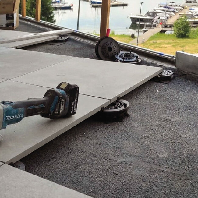 Installation von Außen-Terrassenplatten aus Porzellan auf niedrigprofiligen höhenverstellbaren Kunststoff-Stelzlagern mit einem akkubetriebenen Elektrowerkzeug.