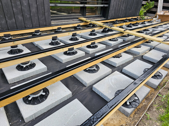 Installation der Terrassen-Unterkonstruktion mit Holzbalken auf höhenverstellbaren Kunststoff-Stelzlagern und Betonfundamentplatten