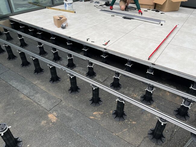 Installation einer erhöhten Außenterrasse mit höhenverstellbaren Kunststoff-Stelzlagern und tragenden Aluminium-Balken mit Keramikplatten.
