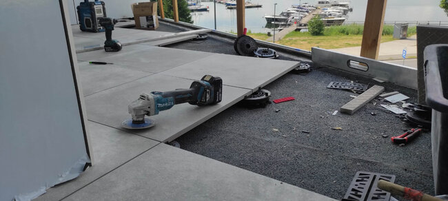 Winkelschleifer-Werkzeug auf erhöhten Terrassenplatten während des präzisen Kantenschneidens auf Stelzlagern.