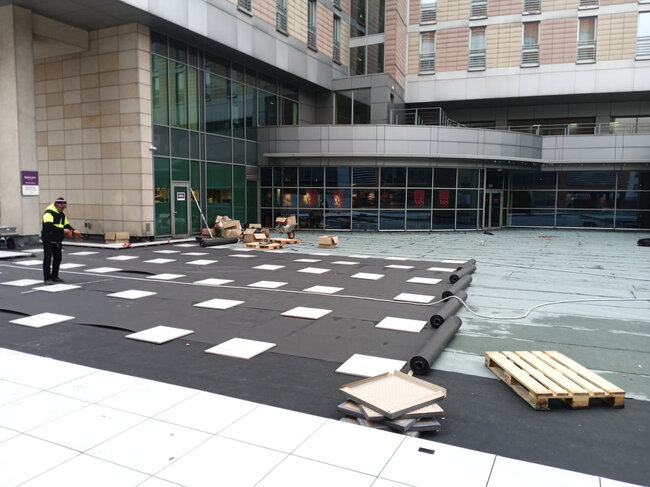 Bauarbeiter, der Terrassen-Stelzlager und eine Grundmembran auf dem Dach eines Gewerbegebäudes installiert.