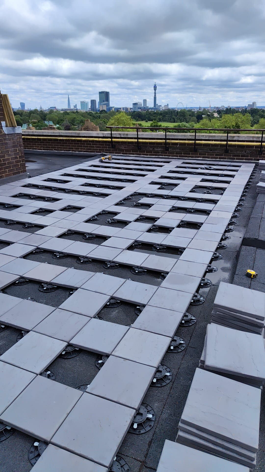 Rastermuster schwerer Betonplatten, teilweise installiert auf höhenverstellbaren Terrassen-Stelzlagern auf dem Dach einer gewerblichen Terrasse.