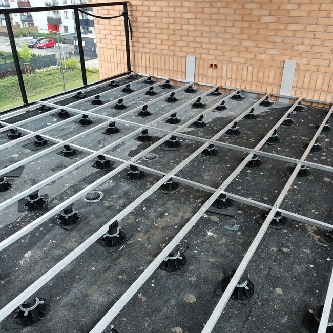 Unterkonstruktion aus einem Raster aus Aluminium-Balken, getragen von höhenverstellbaren Stelzlagern auf einer Dachterrasse.