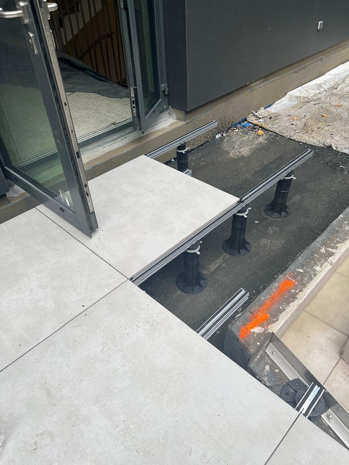 Montage am Terrassentürbereich mit Außen-Porzellanfliesen, die auf Aluminium-Balken und höhenverstellbaren Kunststoff-Stelzlagern verlegt sind.