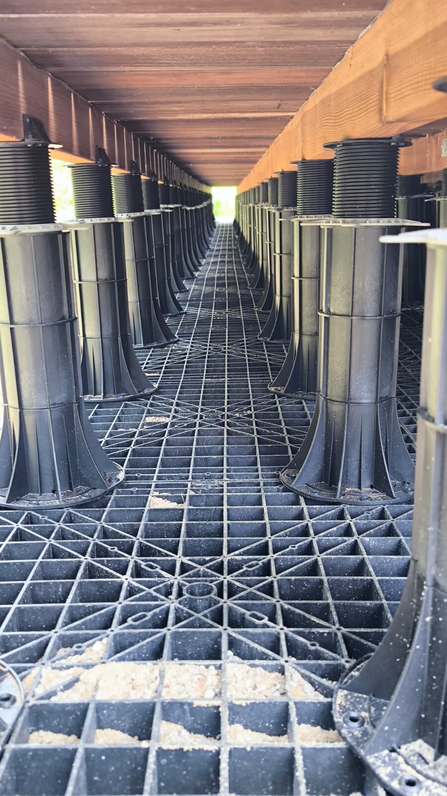 Höhenverstellbares Stelzlager-System aus Kunststoff, installiert unter einer Dachterrassenkonstruktion.