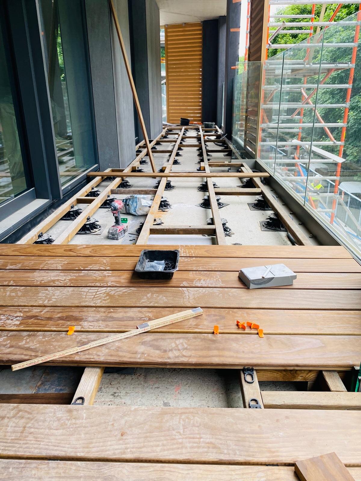 Montage einer Balkonterrasse mit Terrassendielen aus Hartholz, die auf einer höhenverstellbaren Stelzlager-Unterkonstruktion verlegt sind.