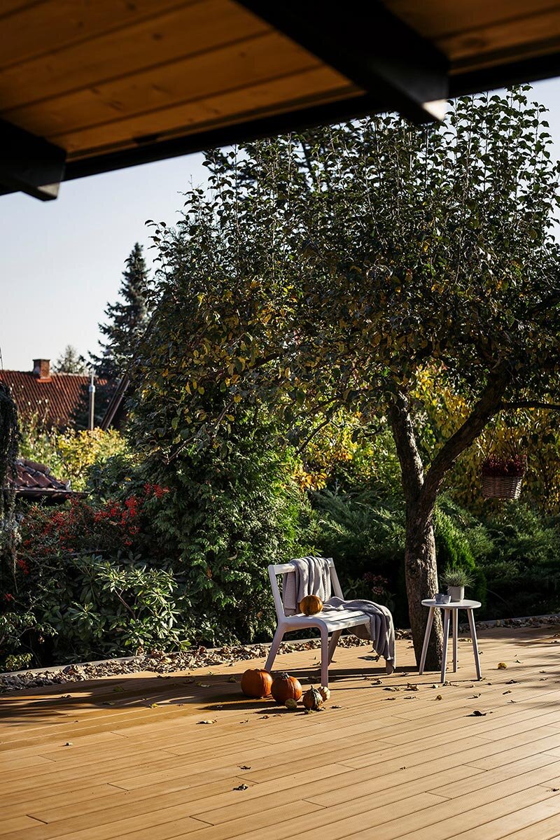 Gemütliche Gartenterrasse mit modernen Verbundholz-Dielen, dekoriert mit Herbstkürbissen und Gartenmöbeln.