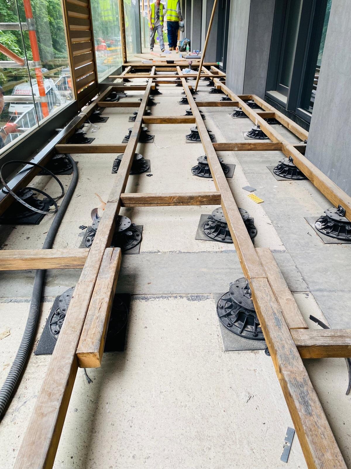 Höhenverstellbare Terrassen-Stelzlager und Holzbalken-Unterkonstruktion, montiert auf einer Balkonterrasse.