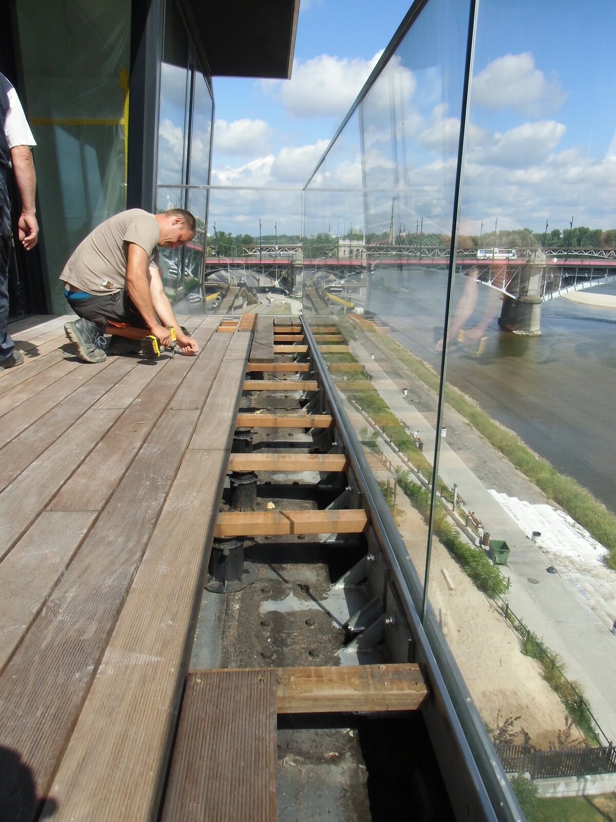 Handwerker, der Terrassendielen auf höhenverstellbaren Terrassen-Stelzlagern auf einem Balkon verlegt.