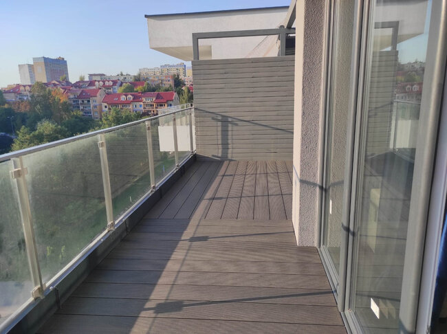 Moderner Apartmentbalkon mit Verbundholz-Dielen, Glasgeländern und Sichtschutz.
