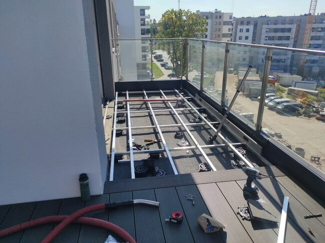 Montage einer Balkonterrasse während der Ausführung mit sichtbarer Konstruktion aus Aluminium-Balken, höhenverstellbaren Stelzlagern und Verbundwerkstoff-Dielen.