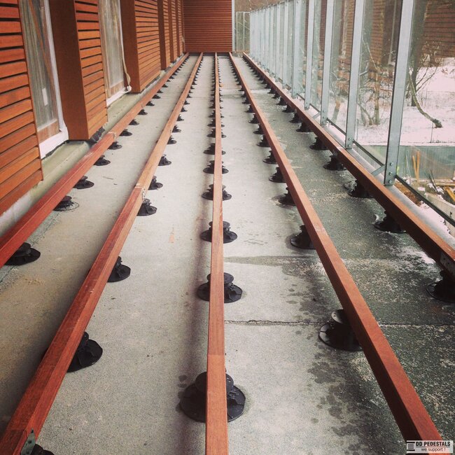 Lange Balkon-Unterkonstruktion mit parallelen Holzbalken, die auf höhenverstellbaren Stelzlagern montiert sind.