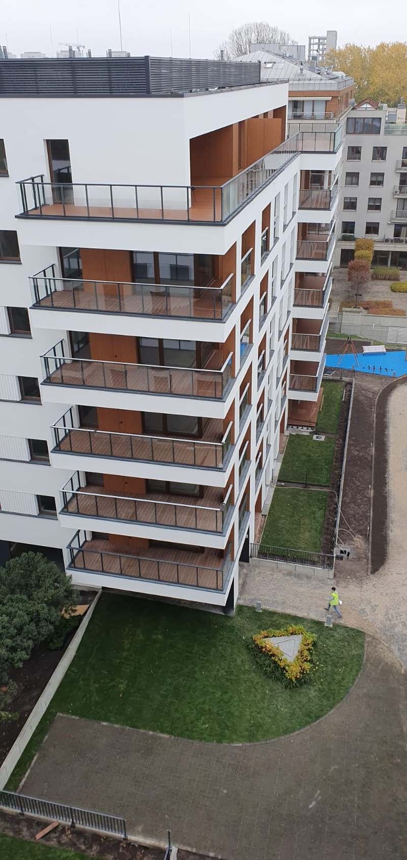 Außenansicht eines modernen mehrstöckigen Wohngebäudes mit holzverkleideten Balkonen und Glasgeländern.