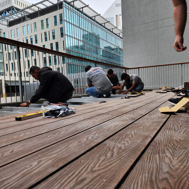 Montage einer Dachterrasse mit Holzdielen auf höhenverstellbaren Stelzlagern und Balken.