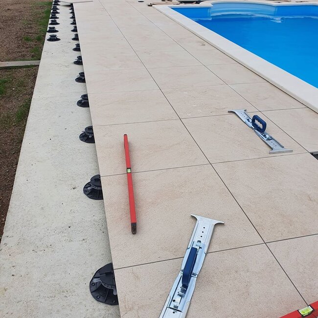 Installation von Feinsteinzeugplatten auf höhenverstellbaren Terrassen-Stelzlagern rund um den Pool.