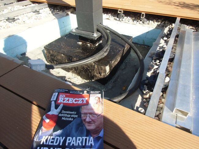 Elektrisches Kabel, das entlang der Basis des Stelzlagers und der darunter liegenden Kiesschicht unter einer erhöhten Stelzlager-Terrasse verlegt ist.
