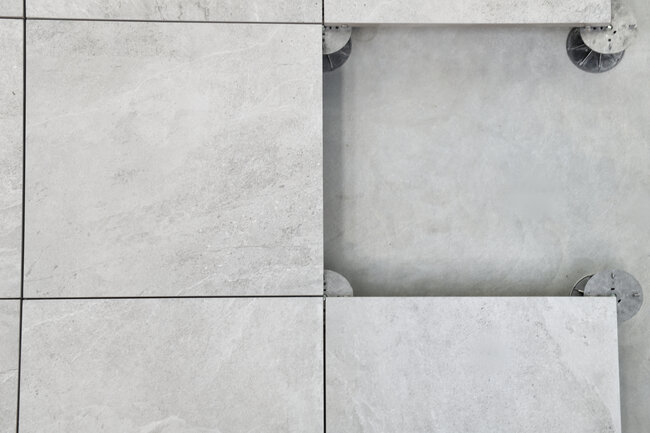 Draufsicht auf Terrassenplatten eines Doppelbodens, die auf Metall-Stelzlagern für Außenbeläge installiert sind.