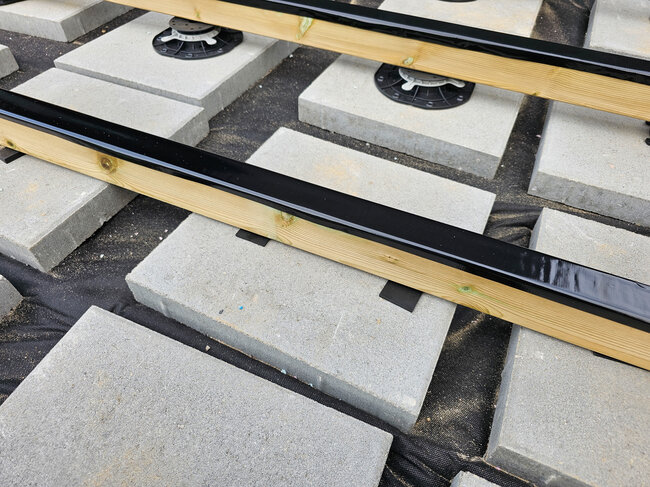 Höhenverstellbare Stelzlager und Fundamente aus Betonplatten, die Holzbalken der Terrasse tragen.