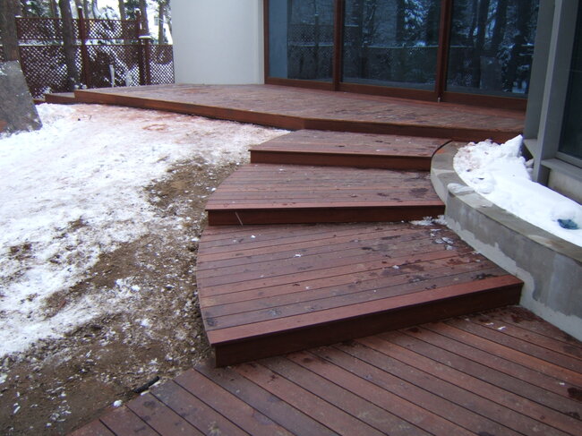 Geschwungene hölzerne Terrassenstufen, die zu einer Außenterrasse führen, die im Winter von Schnee umgeben ist.