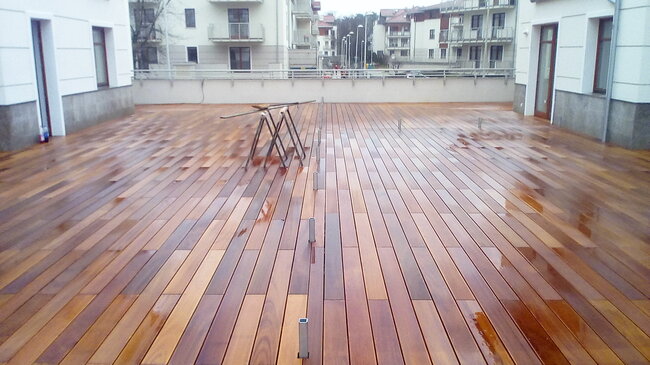 polierte hölzerne Terrassendielen in einem Innenhof einer Wohnanlage mit nassen Dielen und Bauböcken.
