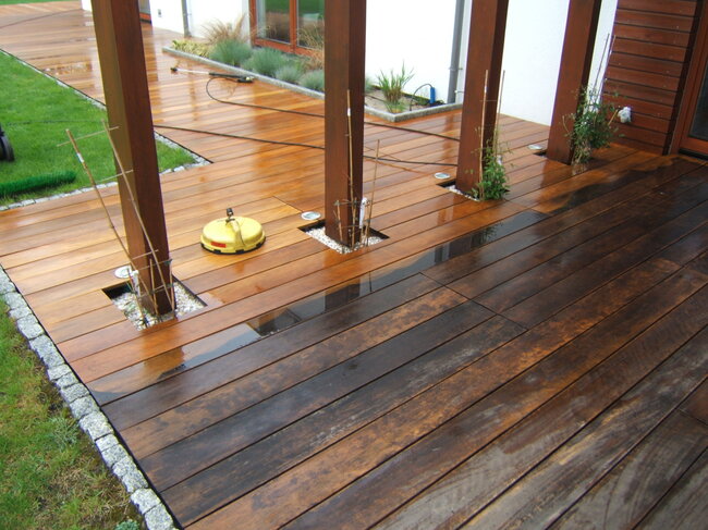 Outdoor wooden deck half-cleaned, showing dark weathered and bright clean boards.