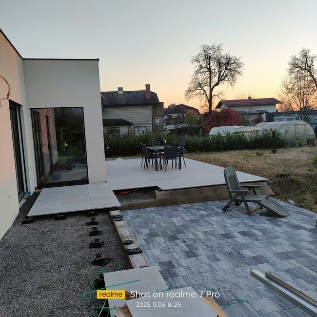 Moderne Patio-Installation mit erhöhten Terrassenplatten, montiert auf höhenverstellbaren Stelzlagern neben einem gepflasterten Abschnitt.