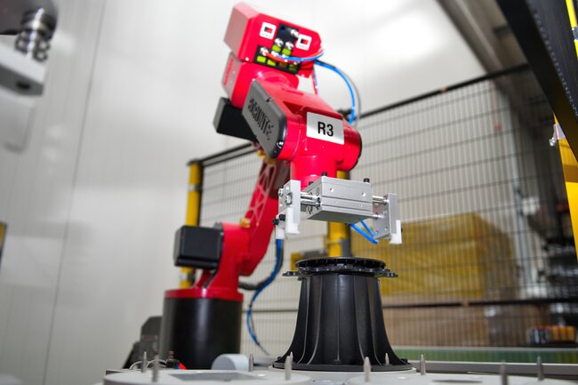 Roter Roboterarm montiert einen schwarzen höhenverstellbaren Terrassen-Stelzlager in einer automatisierten Fabrik.