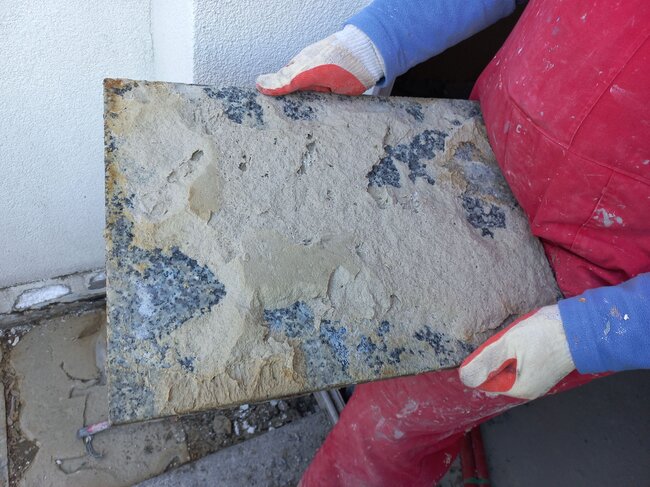 Ein Arbeiter hält eine beschädigte Granitplatte mit Resten von Klebemörtel auf der Unterseite.