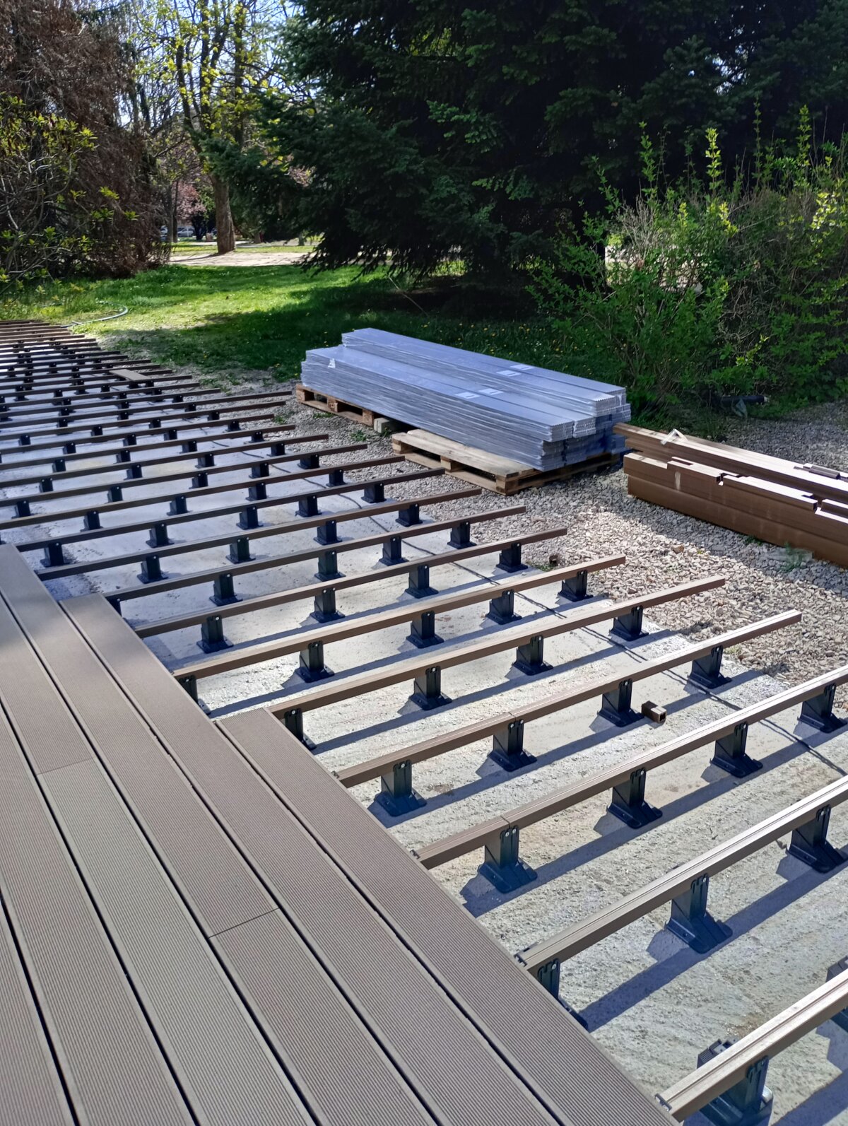 Verbundholz-Terrassendielen, die auf Aluminiumbalken montiert werden, die von höhenverstellbaren Stelzlagern getragen werden.