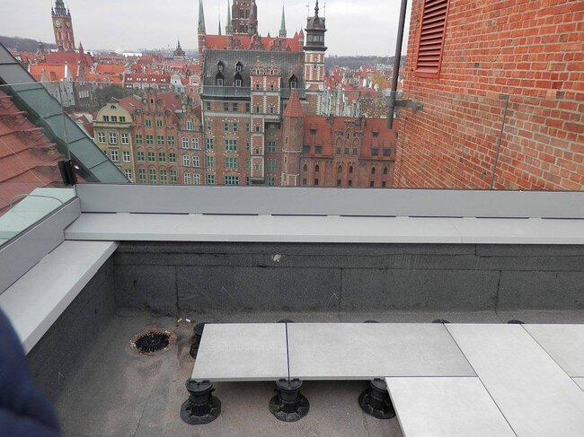 Montage erhöhter Terrassenplatten, gestützt auf höhenverstellbaren Kunststoff-Terrassen-Stelzlagern auf einer Dachterrasse.