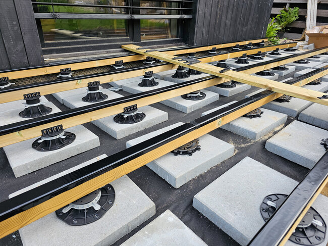 Höhenverstellbare Terrassen-Stelzlager auf Betonplatten, die einen Holzrahmen der Terrasse tragen.