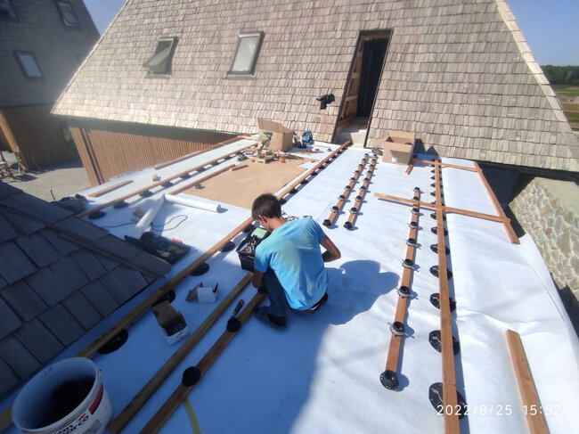 Handwerker installiert höhenverstellbare Terrassen-Stelzlager und Holzbalken auf einer Flachdachmembran.