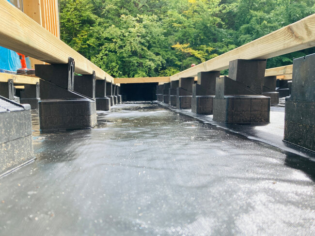 Höhenverstellbare Kunststoff-Terrassen-Stelzlager, die Holzbalken auf einer wasserdichten Dachmembran tragen.