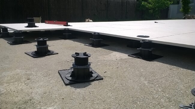 Montage einer erhöhten Terrasse mit höhenverstellbaren Stelzlagern zur Auflage großer Terrassenplatten aus Porzellan.