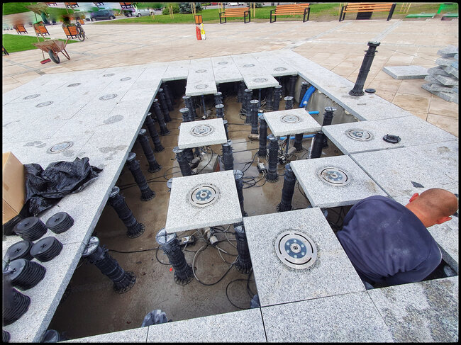 Montage von höhenverstellbaren Stelzlagern und Terrassenplatten mit integrierten Wasserdüsen in einem Trockenbrunnensystem auf der Terrasse.