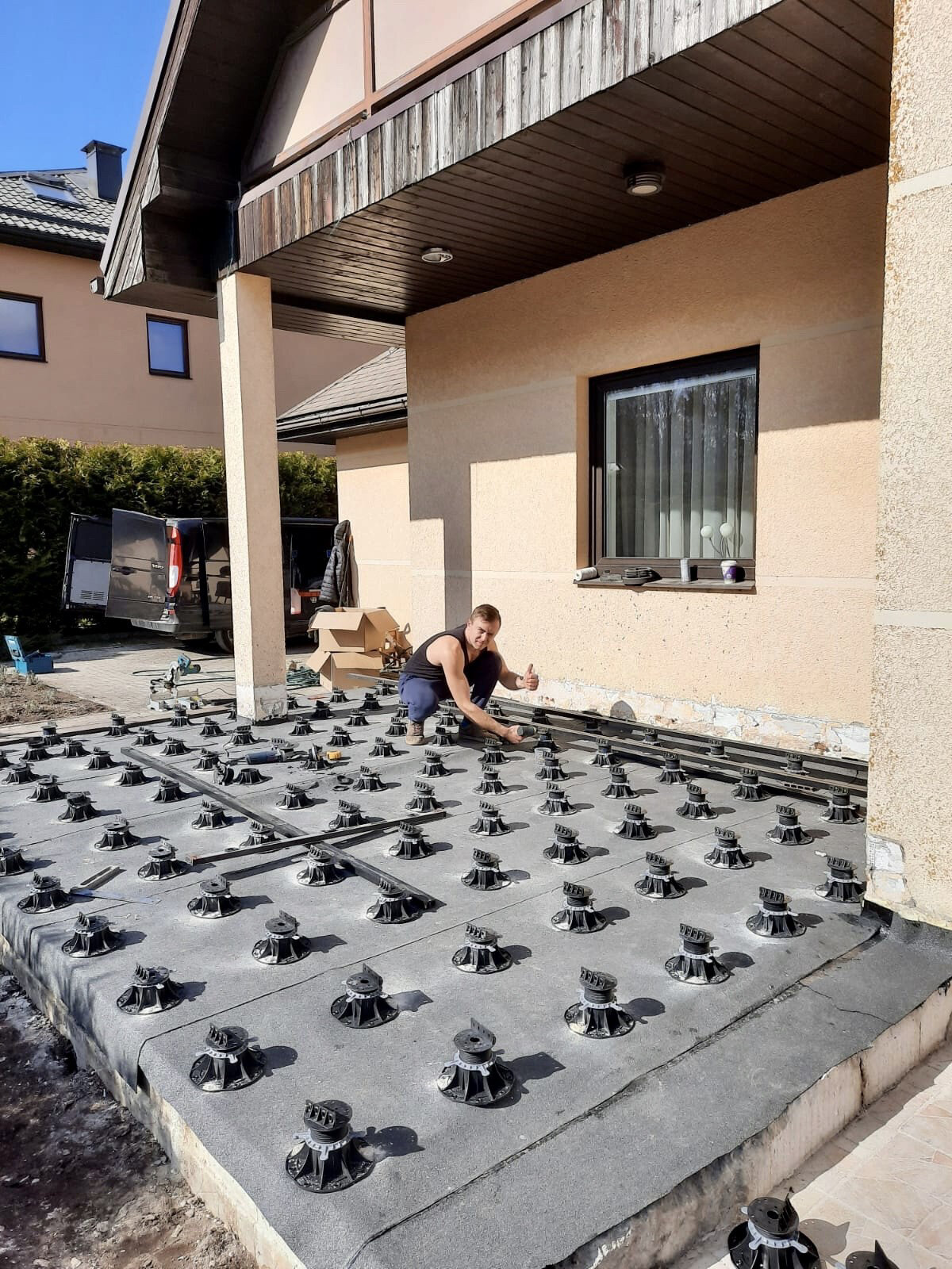 Arbeiter nivelliert höhenverstellbare Stelzlager für den Bau der Balkenunterkonstruktion zur Montage von Verbundwerkstoffdielen.